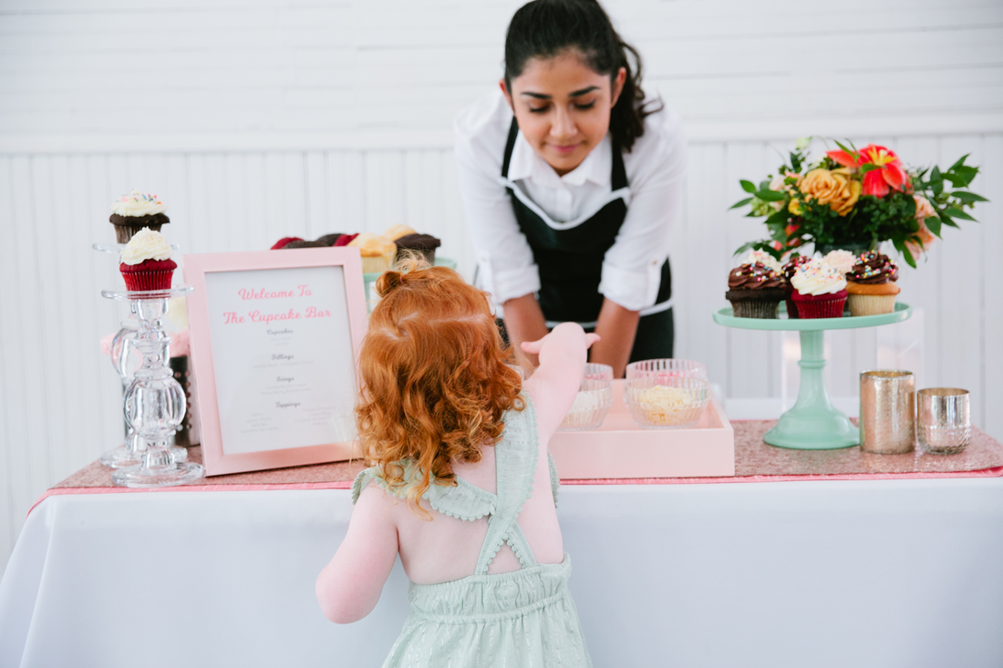 Little girl makes a custom cupcake at an interactive cupcake bar at a wedding in Austin, Texas